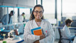 Leinwandbild Motiv Medical Science Laboratory: Beautiful Smart Young Black Scientist Wearing White Coat and Glasses, Holds Test Books, Smiles Looking at Camera. Diverse Team of Specialists. Medium Portrait Shot
