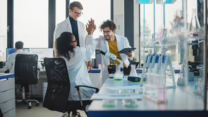 Medical Science Laboratory: Beautiful Black Scientist Discovers New Drug Compound and Celebrate it with High Five. Happy Young Specialists, Doing Innovative Experiments in Advanced Laboratory.