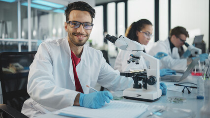 Wall Mural - medical science laboratory: handsome latin scientist analysing samples and uses microscope, looking 