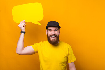 Wall Mural - Happy smiling man with beard in yellow shirt holding empty blank speech bubble.