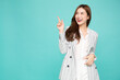 © comzeal - Young Asian woman smiling and pointing finger to empty copy space isolated on green background