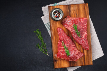 Raw steak on a cutting board with rosemary and spices, dark black background, top view. Fresh grilled meat. Grilled beef steak.