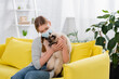© LIGHTFIELD STUDIOS - Young woman with allergy reaction wearing medical mask and holding furry cat on yellow couch