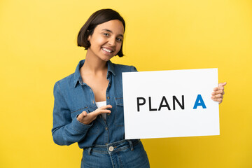 Young mixed race woman isolated on yellow background holding a placard with the message PLAN A and  pointing it