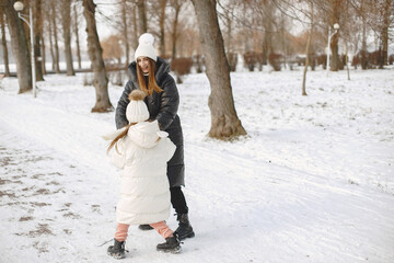 Family in knitted winter hats on family Christmas vacation. Woman and little girl in a park. People walks.