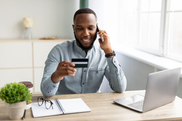 Wall Mural - Black Businessman Holding Credit Card Talking On Cellphone In Office