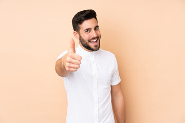 Wall Mural - Caucasian handsome man isolated on beige background with thumbs up because something good has happened