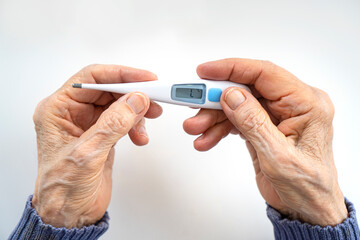 Wall Mural - Old wrinkled hands holding an electronic thermometer for body temperature measurement