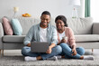 © Prostock-studio - Happy black lovers sitting on carpet at home, using laptop