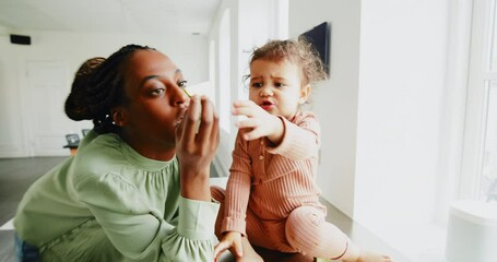 Wall Mural - Loving young African mom and her adorable little girl eating pear slices together in their kitchen at home