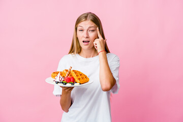 Wall Mural - Young russian woman eating a waffle isolated showing a disappointment gesture with forefinger.