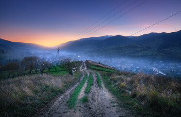 Wall Mural - mountain dirt road at beautiful sunset in summer. colorful landscape with road, village in fog, blue