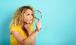 Girl with magnifier lens is distrustful about something. Cyan background