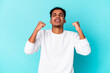 © Asier - Young african american curly man isolated on blue celebrating a victory, passion and enthusiasm, happy expression.