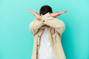 Young caucasian man isolated on blue background keeping two arms crossed, denial concept.