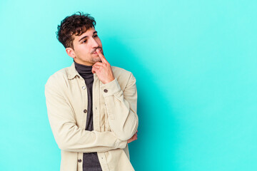 Wall Mural - Young caucasian man isolated on blue background looking sideways with doubtful and skeptical expression.