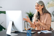 © Kateryna - Happy mature asian woman communicate by video call on computer working from home. Smiling middle aged businesswoman talking by video conference, online virtual meeting using computer