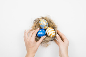 Easter golden decorated eggs in nest with woman hands isolated on white background for web banner. Minimal easter concept. Happy Easter card with copy space for text. Top view, flatlay.