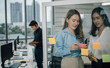 © sticker2you - Asian two woman smiling and using post it notes to share about project.