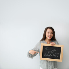 Poster - Young female teacher holding chalkboard with words DO YOU SPEAK ENGLISH? on light background. Space for text