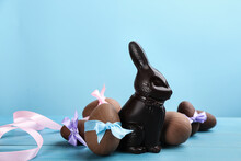 Dark Chocolate Easter Bunny And Eggs On Light Blue Wooden Table. Space For Text