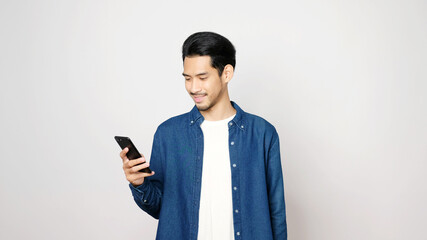 Asian man holding mobile phone smiling while standing isolated on gray background, People on smartphone, technology lifestyle, internet of things concept