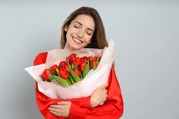 Poster - Happy woman with red tulip bouquet on light grey background, space for text. 8th of March celebration