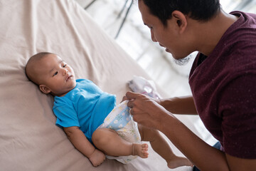 Wall Mural - portrait of asian father changing his infant baby diaper at home