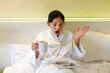 © Missleestocker - Asian woman holding a cup of coffee and laying on bed in the bedroom felling shock after reading the news through tablet on morning day. Furious woman angry about bad news online.
