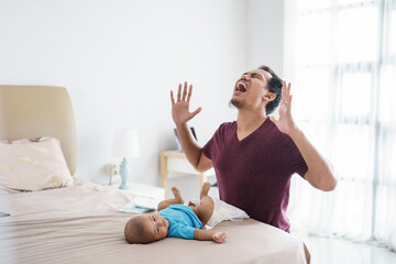 Wall Mural - portrait of stressed asian father changing his infant baby diaper at home