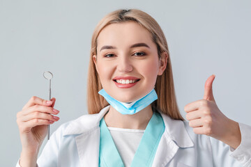 Wall Mural - Female dentist showing thumb-up on light background