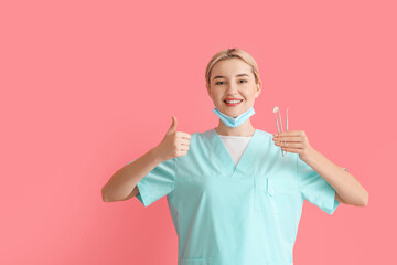 Wall Mural - Female dentist with tools showing thumb-up on color background