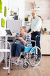 © DC Studio - Disabled senior woman in wheelchair using tablet computer in kitchen with husband near. Paralysied handicapped old elderly person using modern communication online internet web techonolgy.