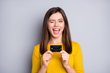 Poster - Portrait of attractive glad cheerful girl holding in hands bank card winking isolated over grey color background