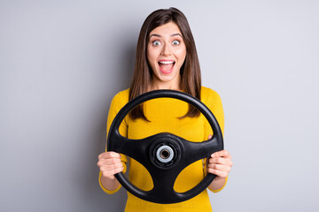 Portrait of pretty amazed cheerful girl holding in hands steering wheel riding auto having fun isolated over grey color background