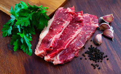 Raw juicy marbled beef steaks with herbs and condiments ready for cooking on wooden table