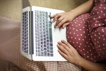 Wall Mural - Pregnant woman sitting on floor and using laptop.