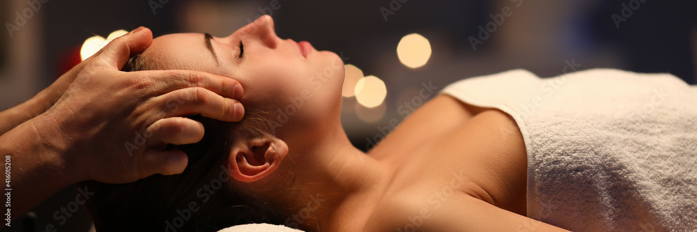 Woman lay on couch on her back with closed eyes and enjoy. Man make relaxing and therapeutic head massage at weight. Spa client has thrown her head back and rejuvenate. Wellness procedures in spa - obrazy, fototapety, plakaty 