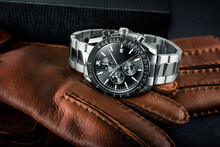 Luxury Stainless Steel Chronograph Watch Resting On A Pair Of Brown Leather Gloves.