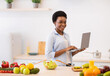 © Prostock-studio - African Lady Holding Laptop Browsing Recipes Cooking Dinner In Kitchen