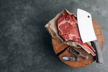 On A Wooden Block For Meat A Fresh Raw Tamahawk Steak Or A Cowboy Steak With A Butcher's Chopping Ax For Meat, Next To It Is A Mixture Of Peppers And Coarse Salt, Milled With Thyme. Fresh Beef Steak