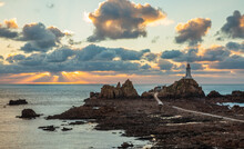 Road To La Corbiere Lighthouse On The Sea Bottom In A Low Tide With Cliff And Sunset,  Bailiwick Of Jersey, Channel Islands