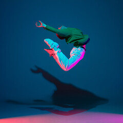 Wall Mural - Flying. Stylish sportive boy dancing hip-hop in stylish clothes on colorful background at dance hall in neon light. Youth culture, movement, style and fashion, action. Fashionable bright portrait.