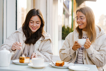 Wall Mural - Two cheerful attractive women friends having tea and cakes