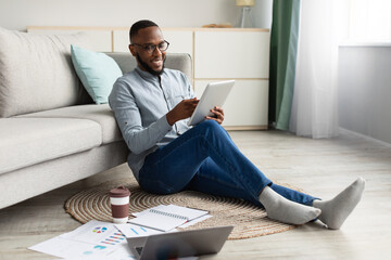 Wall Mural - Happy Black Guy Using Tablet Browsing Internet Sitting At Home