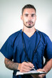 Smiling handsome male doctor in blue scrubs with arms folded in front of white backdrop