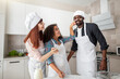 © sofiko14 - Funny multiethnic family preparing pie or cookies in the kitchen, while playing together and enjoy pastime. Cute mixed race girl smearing the flour on her black father's face