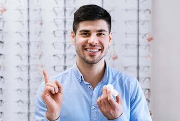 Fototapete - Happy guy holding contact eye lenses in optics shop