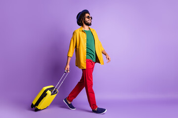 Wall Mural - Full size profile portrait of positive dark skin guy carry suitcase look empty space isolated on purple color background