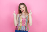 Pretty redhead woman wearing a shiny top standing over pink background showing middle finger doing fuck you bad expression, provocation and rude attitude. screaming excited